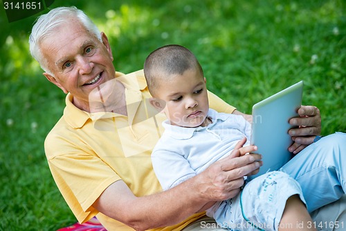 Image of grandfather and child in park using tablet