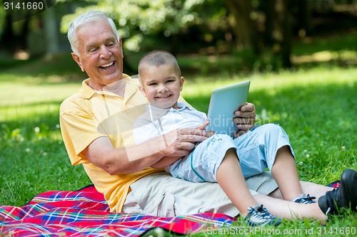 Image of grandfather and child in park using tablet