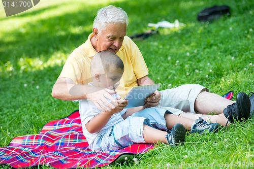 Image of grandfather and child in park using tablet