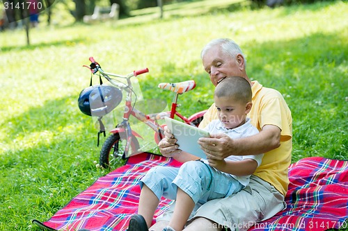 Image of grandfather and child in park using tablet