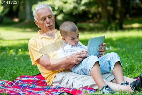 Image of grandfather and child in park using tablet