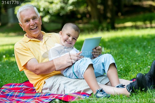 Image of grandfather and child in park using tablet