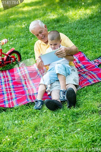 Image of grandfather and child in park using tablet