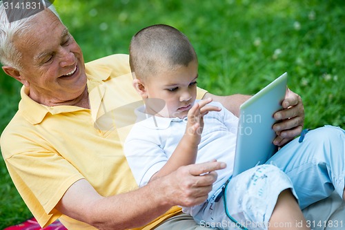 Image of grandfather and child in park using tablet