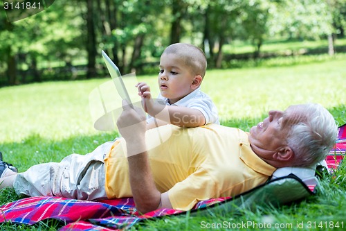 Image of grandfather and child in park using tablet