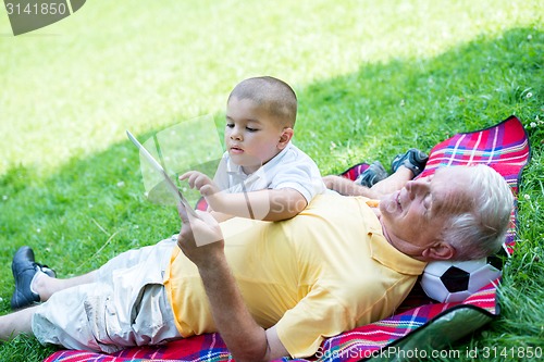 Image of grandfather and child in park using tablet