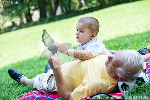 Image of grandfather and child in park using tablet