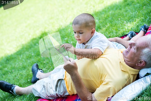 Image of grandfather and child in park using tablet