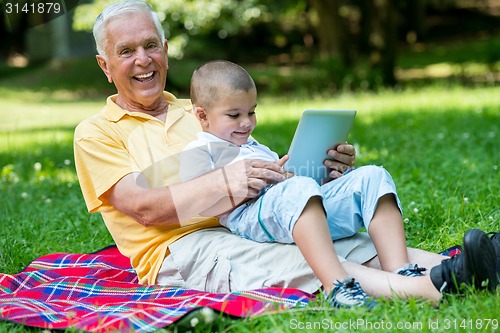 Image of grandfather and child in park using tablet