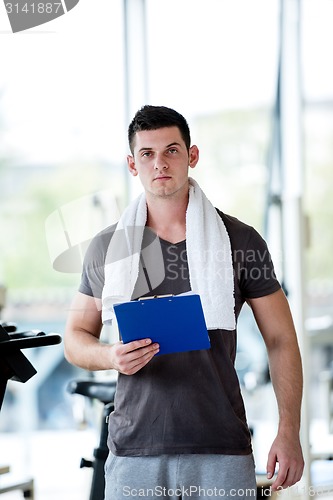 Image of trainer with clipboard standing in a bright gym