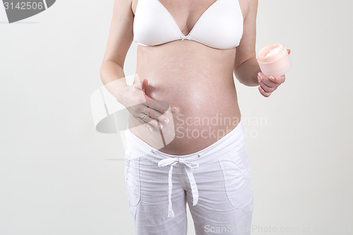 Image of Pregnant woman putting creme on her belly