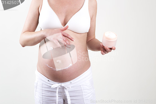 Image of Pregnant woman putting smiley with creme on her belly