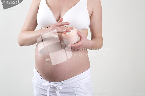 Image of Pregnant woman putting creme on her belly