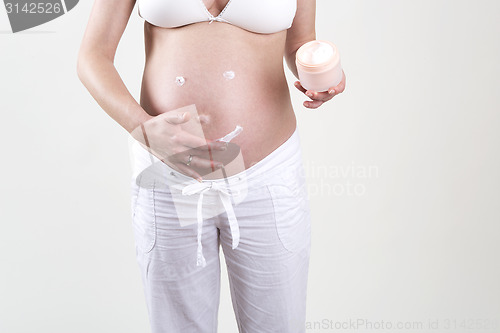 Image of Pregnant woman putting smiley with creme on her belly