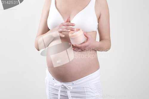 Image of Pregnant woman putting creme on her belly