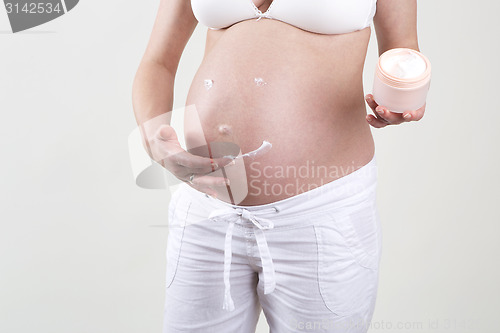 Image of Pregnant woman putting smiley with creme on her belly