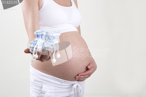 Image of Pregnant woman holding blue baby shoes in her hands