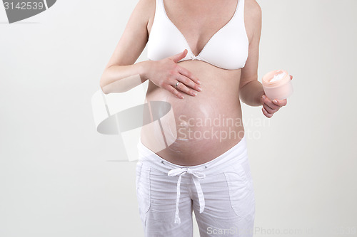 Image of Pregnant woman putting creme on her belly