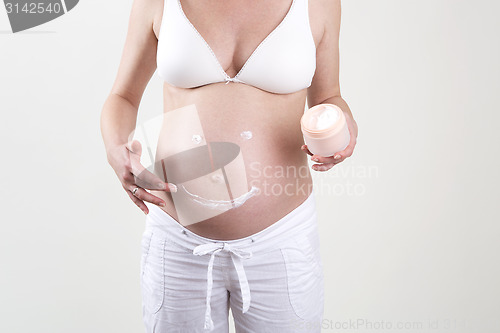 Image of Pregnant woman putting smiley with creme on her belly