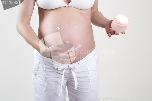 Image of Pregnant woman putting smiley with creme on her belly