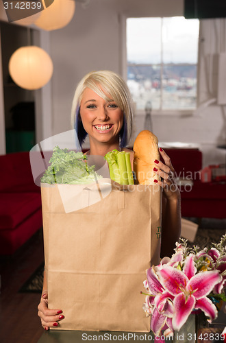 Image of Attractive Female Homemaker Sets Grocery Bag on Counter