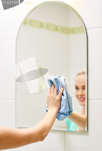 Image of close up of happy woman cleaning mirror with rag