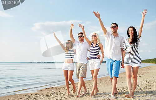 Image of smiling friends walking on beach and waving hands