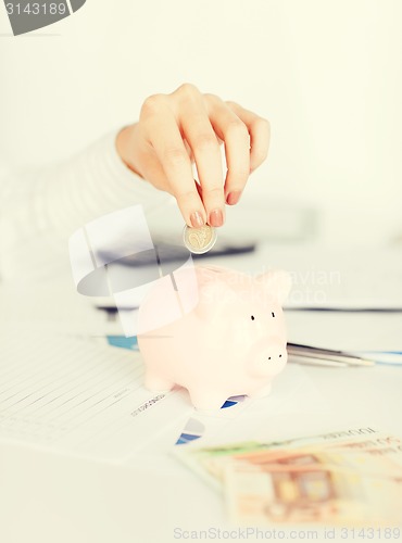 Image of woman hand putting coin into small piggy bank