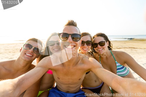 Image of group of smiling friends making selfie on beach