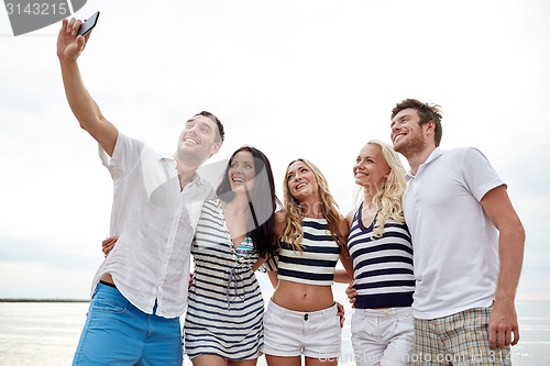 Image of happy friends on beach and taking selfie