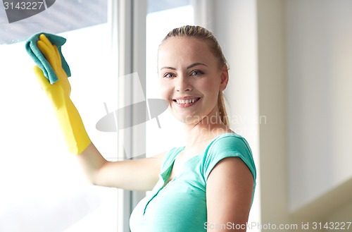 Image of happy woman in gloves cleaning window with rag