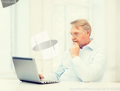 Image of old man in eyeglasses working with laptop at home