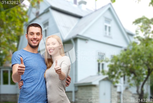 Image of smiling couple showing thumbs up over house