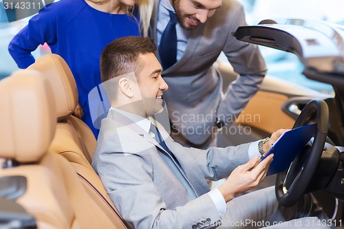 Image of happy couple with car dealer in auto show or salon