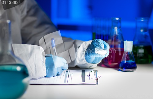 Image of close up of scientist writing test results in lab