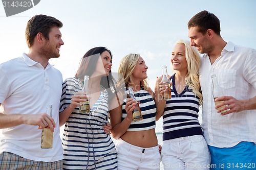 Image of smiling friends with drinks in bottles on beach