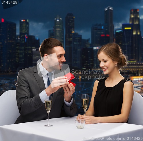 Image of smiling couple with red gift box at restaurant