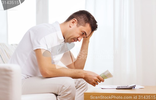 Image of man with money and calculator at home