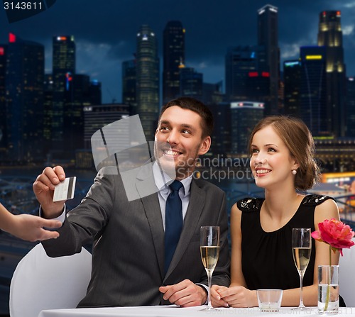 Image of smiling couple paying for dinner with credit card