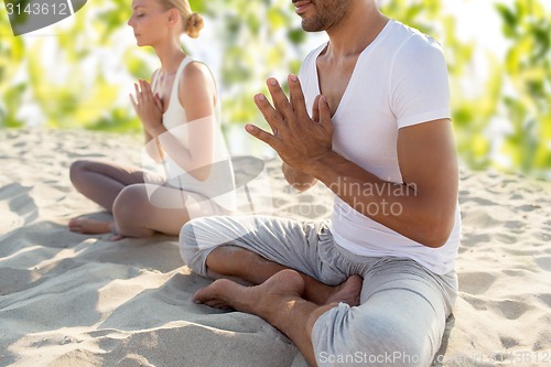 Image of smiling couple making yoga exercises outdoors