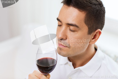 Image of happy man drinking red wine from glass at home