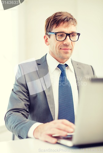 Image of businessman in eyeglasses with laptop in office