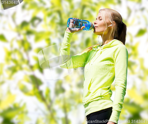 Image of woman drinking water after doing sports outdoors