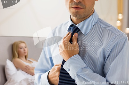 Image of close up of man adjusting tie on neck in bedroom