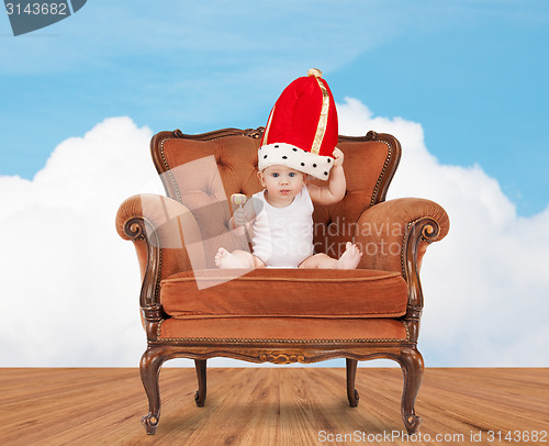 Image of baby in royal hat with lollipop sitting on chair