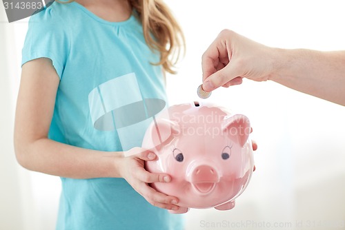 Image of close up of girl with piggy bank putting coin