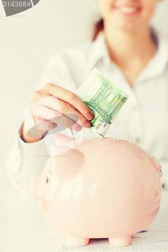 Image of woman puts euro cash into large piggy bank