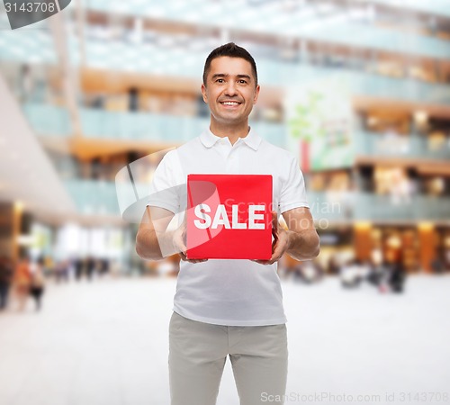 Image of smiling man with sale sigh over mall background