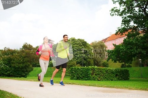 Image of smiling couple with earphones running outdoors