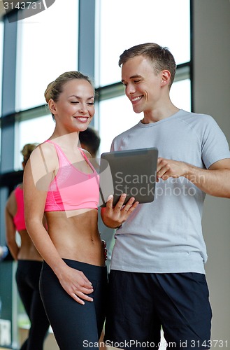 Image of smiling young woman with personal trainer in gym